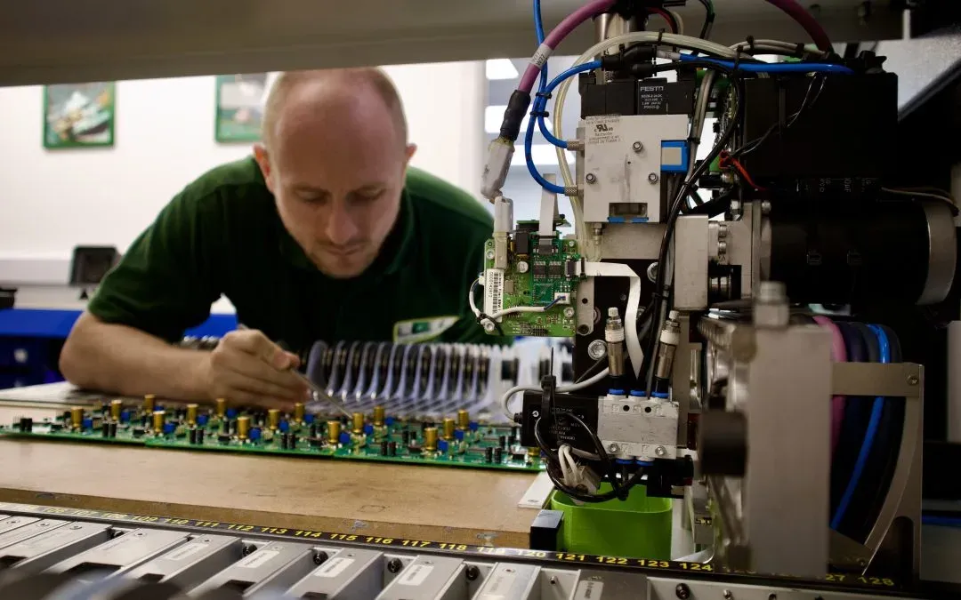 Technician inspecting printed circuit board during automated PCB assembly process in electronics manufacturing